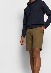 Marineblauer Kapuzenpullover mit Fronttasche und Kordelzug, kombiniert mit olivgrünen Shorts. Die Shorts haben einen geraden Schnitt und Fronttaschen.