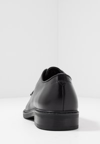 Chaussure de ville en cuir noir avec une forme arrondie, une texture lisse et un petit talon. Présente des détails de couture et un design élégant.