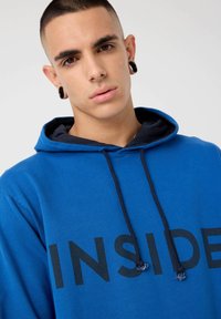 Sudadera azul con un estampado negro de "INSIDE", cordones con extremos texturizados y una capucha interior en capas de color navy. Tejido suave con un corte relajado.