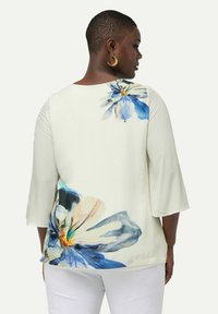 Blomsterbluse med trekvartærmer, prydet med store blå og ferskenfarvede blomster på en cremet baggrund. Blødt stof med en afslappet pasform.