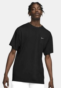 Tricou negru cu mânecă scurtă, realizat din bumbac, cu un guler rotund și un mic logo alb Nike pe piept. Design lejer.