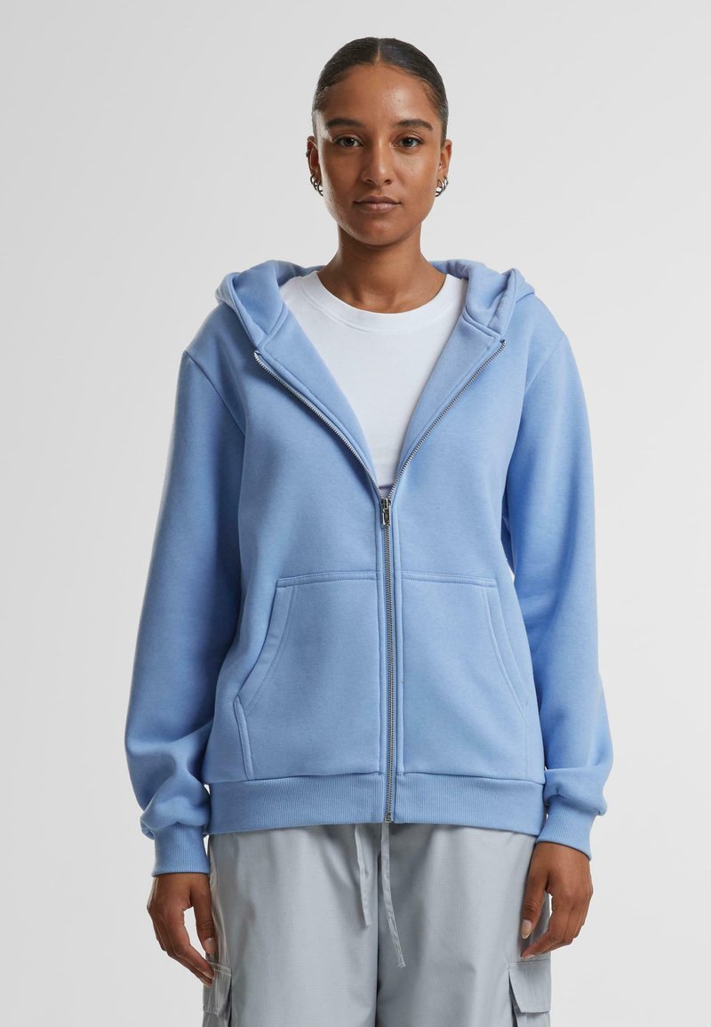 Felpa con zip di colore blu chiaro, realizzata in tessuto morbido, con una zip frontale, due tasche e cappuccio con coulisse. Texture liscia e vestibilità comoda.