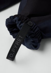 Marineblåt stof med gathered elastisk åbning, der har en sort rem med præget tekst og en sort knap på siden til fastgørelse.