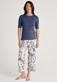 Marineblauw t-shirt met korte mouwen, gecombineerd met witte, gestreepte wijde broek die blauwe en gouden hemelontwerpen en palmbomenmotieven bevat.