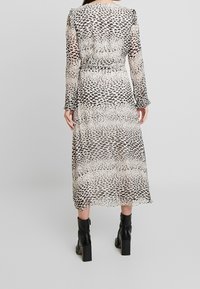 Maxikleid aus transparenter Stoff mit einem schwarz-beigen Tierdruck, langen Ärmeln, Rüschensäumen und einer definierten Taille, kombiniert mit kniehohen schwarzen Stiefeln.