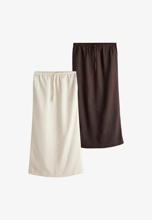 Frau geht drinnen, trägt ein schwarzes T-Shirt, einen dunkelbraunen Rock, schwarze Sandalen und trägt eine schwarz-weiß gestreifte Einkaufstasche.