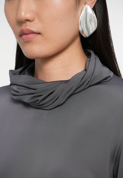 Grå trøje med cowl neck i blødt, glat stof; parret med en stor, sølvfarvet ørering i en organisk form med en poleret finish.
