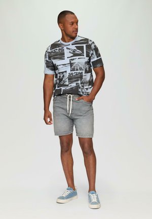 Zwart en lichtblauw graphic t-shirt met korte mouwen en collagedrukken, gecombineerd met lichtgrijze shorts en blauwe sneakers met witte veters.