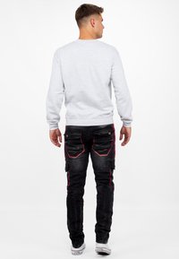 Un sweat-shirt gris associé à un jean cargo noir avec des coutures rouges, des poches zippées et une finition texturée. Des chaussures décontractées complètent le look.