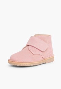 Bota de tobillo de ante rosa con una amplia correa de Velcro, punta redondeada y suela de madera clara. Textura suave y diseño sencillo.