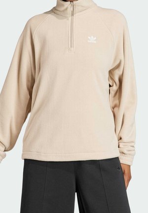 Beige quarter-zip fleece pullover with Adidas logo on chest, worn with black Adidas pants, fabric soft and loose-fitting.
