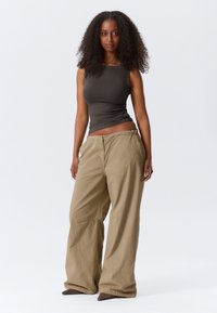 Olīvzaļš bezroku tops, kombinēts ar vaļīgām plašu kāju khaki krāsas biksēm. Biksēm ir strukturēts, ribots dizains ar elastīgu jostasvietu.