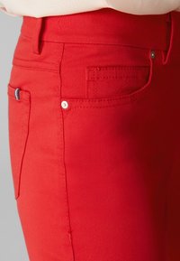 Pantalons en denim rouge avec une taille standard, des poches latérales et des détails en métal contrastants, le tout dans une texture lisse.