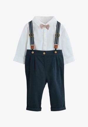 Navyblauwe overalls met opgerolde pijpen, verstelbare gestreepte bretels en een wit overhemd met een lichtroze strik.