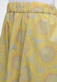 Jupe avec taille élastique présentant un motif de tournesols jaunes sur fond clair, portée avec un haut blanc.