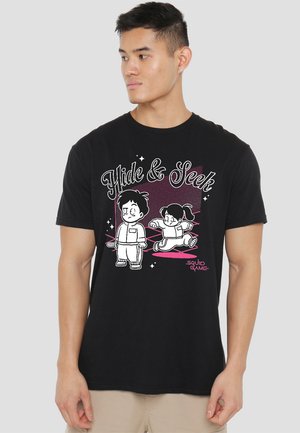 Black cotton t-shirt featuring white cartoon graphics of two characters playing hide and seek, with pink accents and "Squid Game" text.