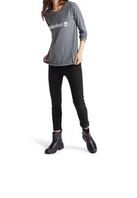 Gray long-sleeve t-shirt with "Timberland" logo, paired with black skinny pants and black ankle boots with a textured finish.