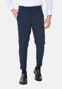 Pantaloni blu navy con vestibilità su misura, dotati di tasche laterali, vita piatta e orli a risvolto, abbinati a mocassini neri e una camicia bianca.