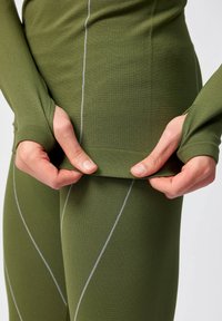 Olijfgroene sportoutfit met textuur, een aansluitende pasvorm en grijze contrasterende naden langs de mouwen en taille.