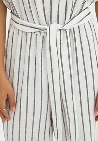 Tuta a righe caratterizzata da un tessuto bianco testurizzato con sottili strisce nere, vita con cintura e design morbido.