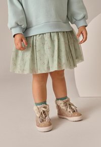 Pulover albastru deschis, fustă plisată florală verde mentă, și adidași bej cu accente pufoase și șireturi, asortați cu șosete turcoaz.