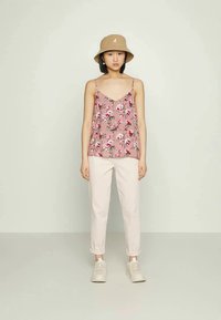 Top floral em rosa com alças finas, combinado com calças brancas até aos tornozelos e ténis claros. Modelo usa um chapéu de balde bege.