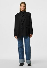 Blazer nero oversize con due tasche frontali e due bottoni, abbinato a jeans in denim a gamba larga con orlo sfilacciato di colore azzurro chiaro.