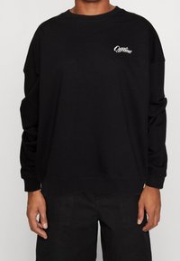 Persona vestida con una camiseta de manga larga negra que tiene impresa en blanco la palabra "Offline" y un icono de señal en la parte superior izquierda del pecho.