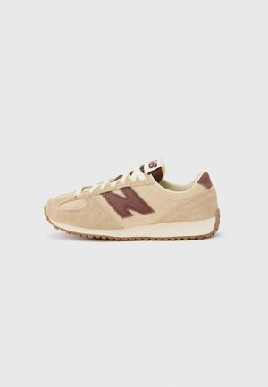 Sneaker in camoscio beige con logo accentuato marrone, lacci color crema e suola in gomma texturizzata. Presenta un design a profilo basso e punta arrotondata.