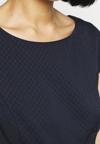 Námořnická modrá texturovaná šaty s širokým kulatým výstřihem a krátkými rukávy, s jemným vzorem malých čtverečků.