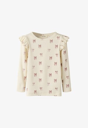 Top de manga larga color crema con textura acanalada, que presenta un patrón de lazo rosa repetido y detalles con volantes en los hombros.