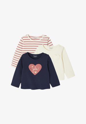 Drei Langarmshirts: eines in Marineblau mit einem Herz-Graphic, eines in Creme mit einer Herzumrandung und eines mit roten Streifen auf weißem Stoff.