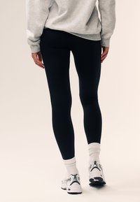 Mustad venivad püksid, millel on kehalikku sobivust rõhutav disain. Paari kuuluvad valged ja hallid spordijalatsid ning soonikkoes valged sokid.