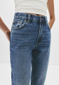 Blauwe denim hoge taille jeans met een relaxte pasvorm, voorzien van voorzakken, contrasterende stiksels en een knoopsluiting bij de taille.