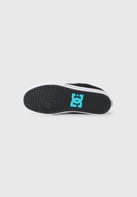 Suela de zapatilla negra con ribete blanco y un logo azul de DC centrado en el patrón de la superficie texturizada sobre un fondo blanco liso.