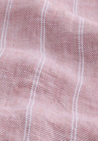 Textiltyg i en ljusrosa nyans med fin väv, med vita vertikala ränder och en mjuk textur.