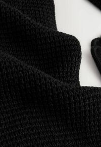 Čierna pletená tkanina so štruktúrovaným, vaflovým vzorom, s jemným a chlpatým povrchom. Detailný záber, ktorý zvýrazňuje jej detaily.