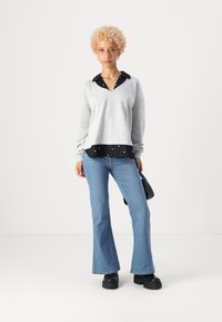 Sweat-shirt gris en V avec un col noir et des pois décoratifs, associé à un jean flare bleu clair et des chaussures à plateforme noires.