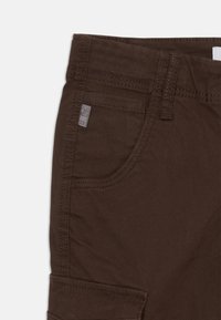 Bruine katoenen cargobroek met een zijzak, stevige stiksels en een gestructureerde afwerking. Inclusief een klein merkje op de tailleband.