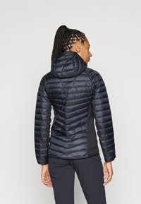 Sort pufferjakke med en tætsiddende design, der har hætte og quiltet tekstur. Sidelapper i et kontrasterende materiale for ekstra stil.