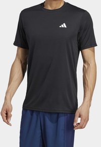 Mustat urheilupaidat, jotka on valmistettu hengittävästä kankaasta, pyöreällä kaula-aukolla, lyhyillä hihoilla ja vasemmassa rinnassa valkoisella logolla.