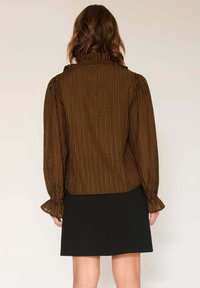 Blouse rayée marron avec un col haut, des manches bouffantes et des poignets à volants, associée à une jupe noire. Texture lisse, design ajusté.