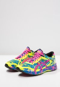 Des chaussures de sport arborant un schéma de couleurs vif en jaune, bleu et rose, avec une tige en mesh, une semelle crantée et des lacets roses.