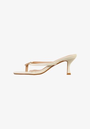 Kremfarvet højhælet thong-sandal med en tynd rem og dekorativ spænde foran, med en slank mellemhøj hæl.