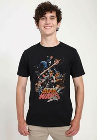 T-shirt en coton noir avec un graphique multicolore "Star Wars", représentant des personnages et des vaisseaux spatiaux dans un design rétro. Manches courtes, col rond.