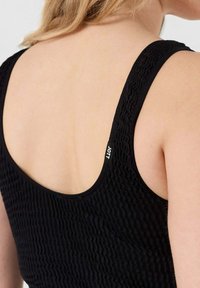 Zwarte mouwloze top met een gestructureerd, geribbeld ontwerp. De achterkant heeft een scoopvorm met een klein logo-label nabij de schouder.