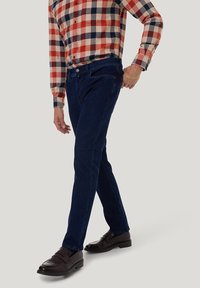 Donkerblauwe jeans met een slim fit, met een gladde textuur en een standaard vijf-pocket ontwerp. Gepaarde met een geruit overhemd met knopen.
