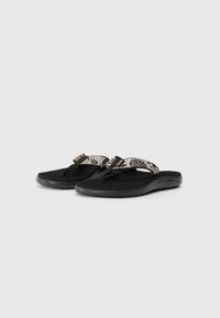 Zwarte slippers met een gestructureerde zwarte zool, voorzien van een gestreepte stoffen band in wit en zwart, met een logo-accent in oranje.