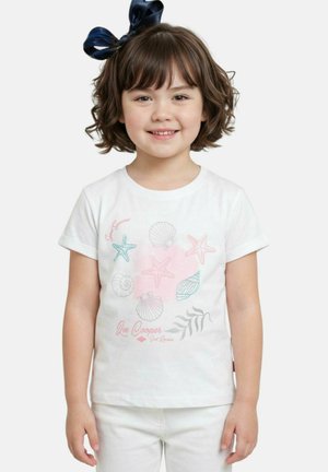Jeune fille souriante aux cheveux bruns courts et portant un nœud bleu marine, vêtue d'un t-shirt blanc orné de motifs pastel de coquillages et d'étoiles de mer.
