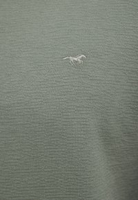 Tkanina o szarej teksturze z małym białym haftem przedstawiającym konia po lewej stronie. Materiał ma pleciony wzór.